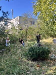 Kinder und Erwachsene pflegen Garten in Graz-Nord mit moderner Architektur im Hintergrund.